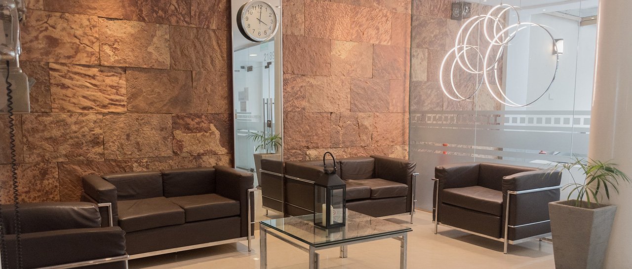 El lobby con la pared de piedra, los sillones de cuero y el reloj