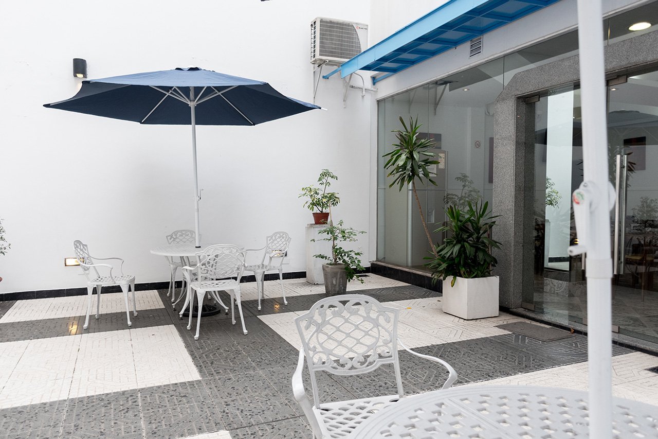 El patio del hotel con sombrilla azul y mesas de jardín blancas